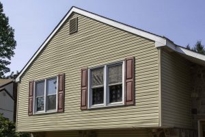 Tan siding on home with two windows and red shutters